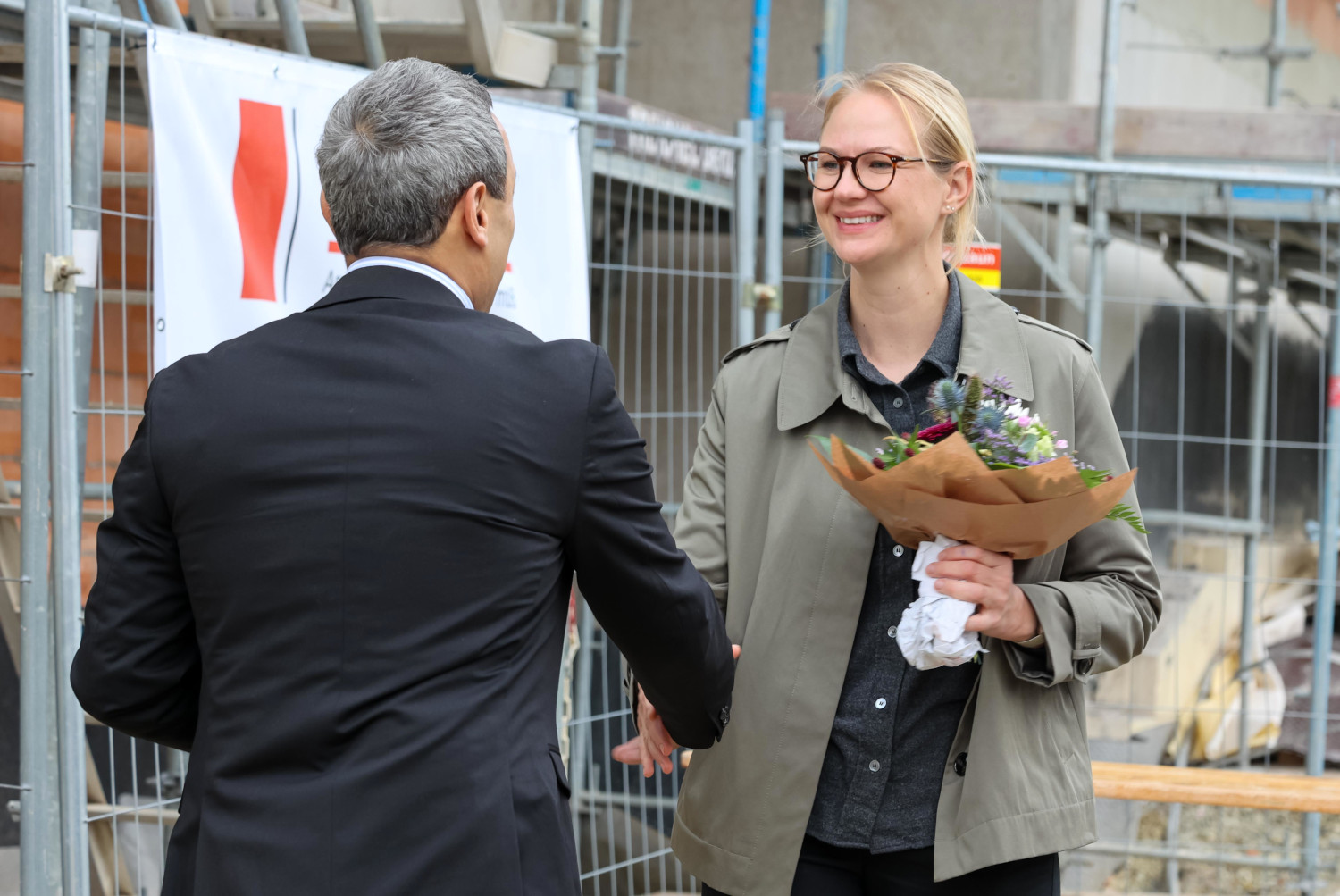 Eine Frau hält einen Blumenstrauß in der Hand. Davor steht ein Mann und gratuliert der Frau.