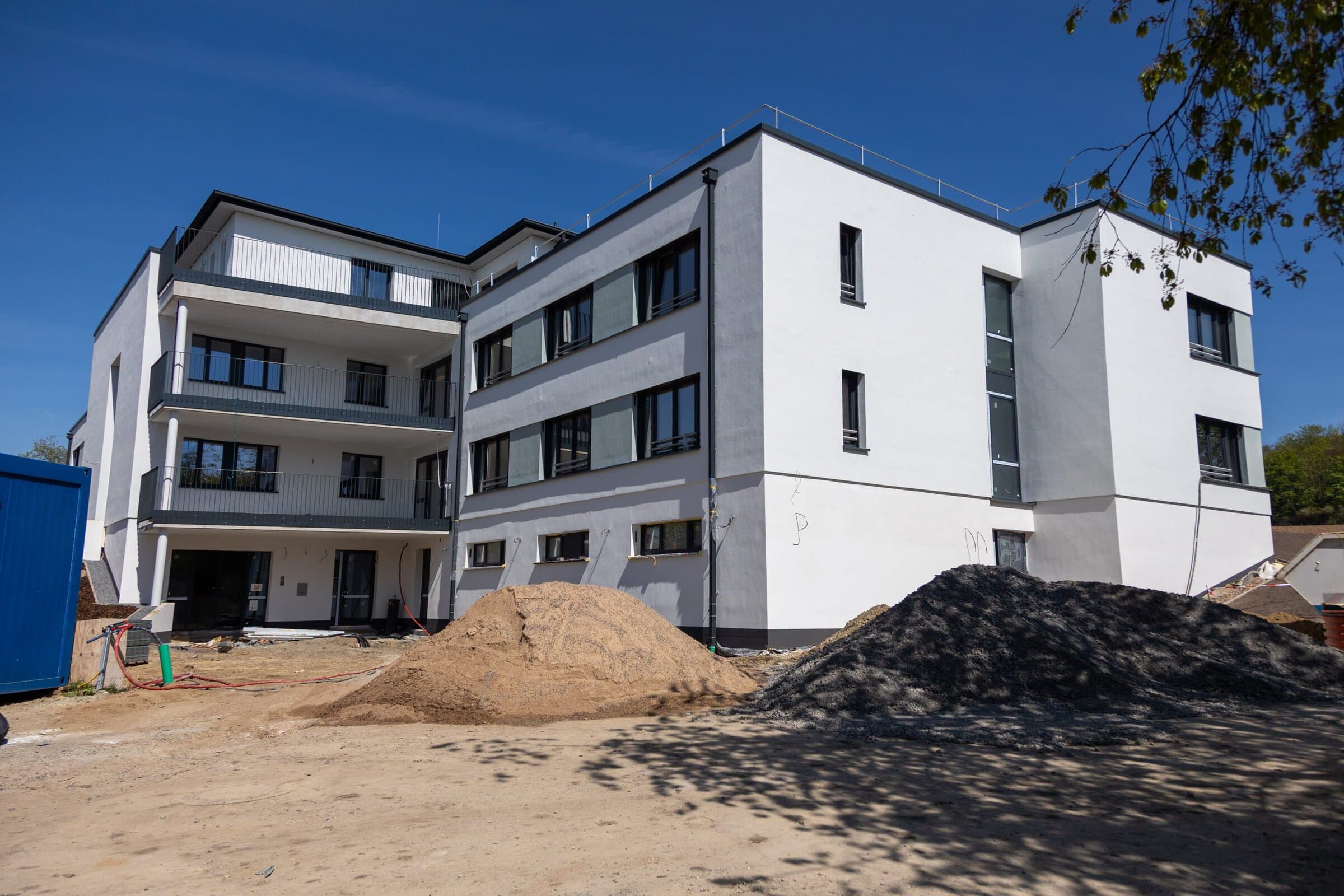 Ein neues, großes, weißes Haus steht bei strahlendem Sonnenschein inmitten einer Baustelle.